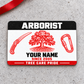 Arborist Red Monochrome aluminum wallet card, front view on gray concrete with a red ribbon.