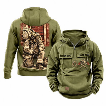 Firefighter Ready Every Day Portrait Vintage Hoodie in Military Green, shown from front and back on white. The half-zip front has CUSTOM NAME and SINCE 2000 sample tabs, helmet-and-crossed-axes chest artwork, plain sleeves and lower pouch with a small brown label. The back shows a compact firehouse-and-hose panel above a larger kneeling firefighter beside a closed equipment bag.