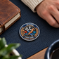 Silver HVAC legacy-laurel challenge coin on a home desk mat beside a journal