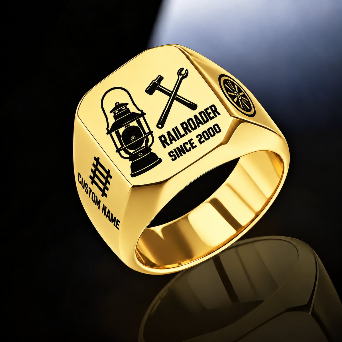 Gold Railroader Split Emblem ring with an asymmetric railway lantern and crossed railway-tool composition, with the name on the left shoulder below a track motif and a rail-wheel emblem on the right shoulder, with illustrative CUSTOM NAME and SINCE 2000 artwork