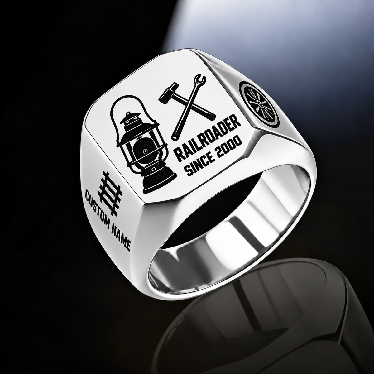 Silver Railroader Split Emblem ring with an asymmetric railway lantern and crossed railway-tool composition, with the name on the left shoulder below a track motif and a rail-wheel emblem on the right shoulder, with illustrative CUSTOM NAME and SINCE 2000 artwork