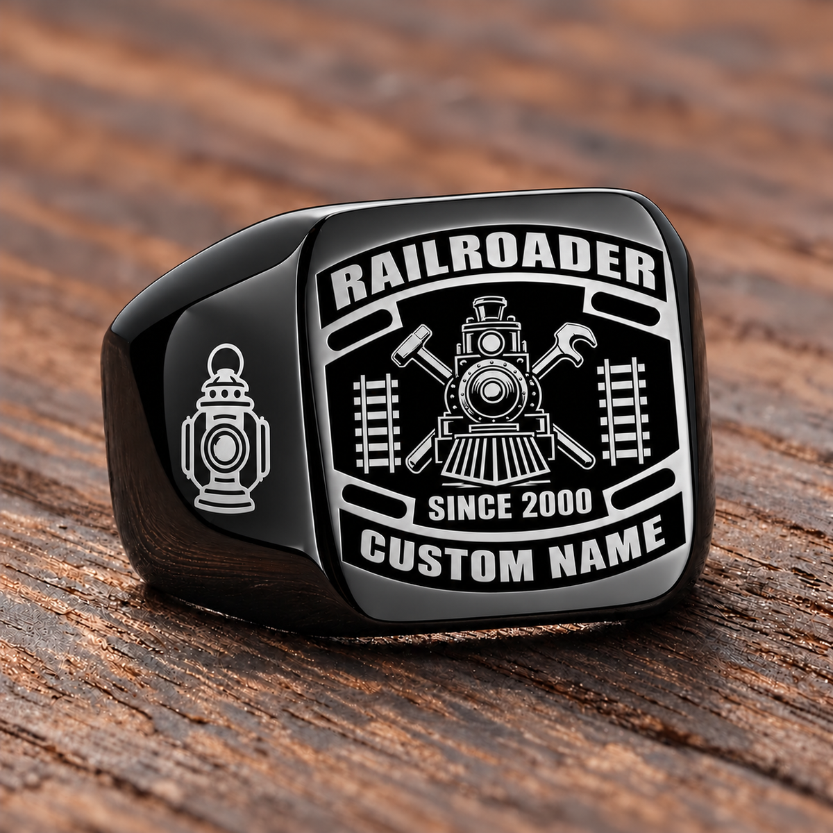 Black Railroader Black Face Badge ring with a black badge-style face with a locomotive over crossed railway-tool silhouettes, flanking track motifs and a railway lantern on the left shoulder, with illustrative CUSTOM NAME and SINCE 2000 artwork