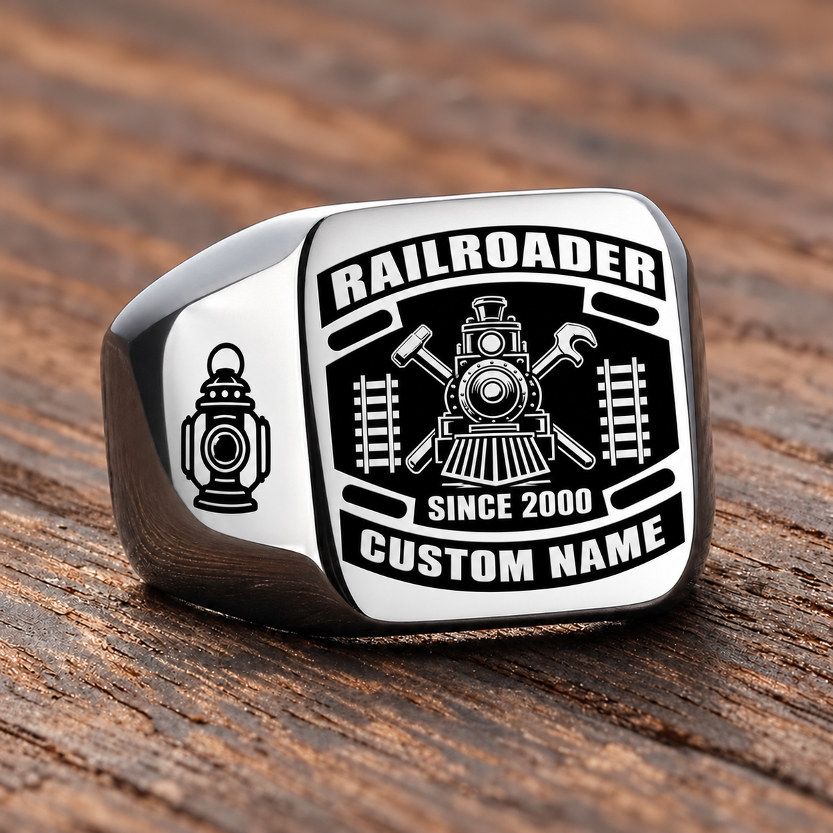 Silver Railroader Black Face Badge ring with a black badge-style face with a locomotive over crossed railway-tool silhouettes, flanking track motifs and a railway lantern on the left shoulder, with illustrative CUSTOM NAME and SINCE 2000 artwork
