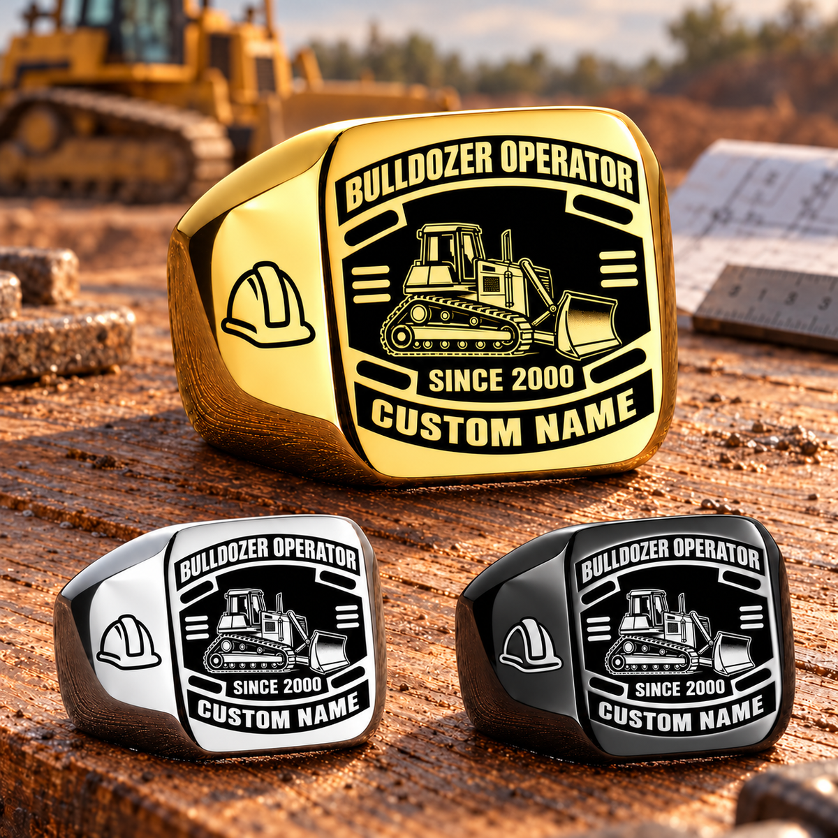Gold-led triangular arrangement of Bulldozer Operator Black Face Badge rings in Gold, Silver and Black on a heavy-equipment maintenance workbench, with tracked bulldozer and hard-hat artwork and sample CUSTOM NAME and SINCE 2000 engraving.
