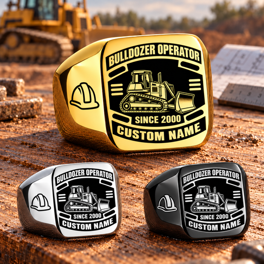 Gold-led triangular arrangement of Bulldozer Operator Black Face Badge rings in Gold, Silver and Black on a heavy-equipment maintenance workbench, with tracked bulldozer and hard-hat artwork and sample CUSTOM NAME and SINCE 2000 engraving.