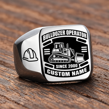 Silver Bulldozer Operator Black Face Badge ring with a tracked bulldozer and front pushing blade on the black face, a hard-hat shoulder motif, and sample CUSTOM NAME and SINCE 2000 engraving.