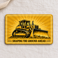 Reverse of the Bulldozer Operator Golden Milestone aluminum wallet card, with a tracked bulldozer and the message SHAPING THE GROUND AHEAD on a golden sunburst, resting on cream linen.