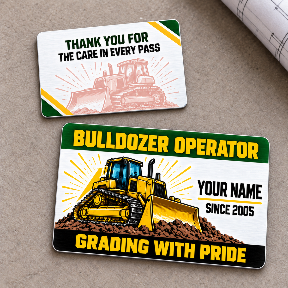 Front and reverse of the Bulldozer Operator Green Band aluminum wallet card on a neutral tabletop, with yellow tracked bulldozer artwork, green header, black Grading with Pride footer and a pale matching thank-you reverse.