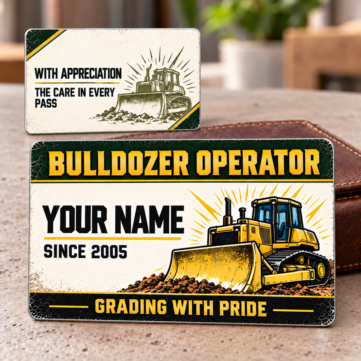 Front and reverse of the Bulldozer Operator Heritage Band aluminum wallet card on a pale tabletop with a brown wallet, showing a left-aligned sample name, yellow tracked bulldozer with front blade, dark-green header, black footer and matching cream-and-olive appreciation reverse.