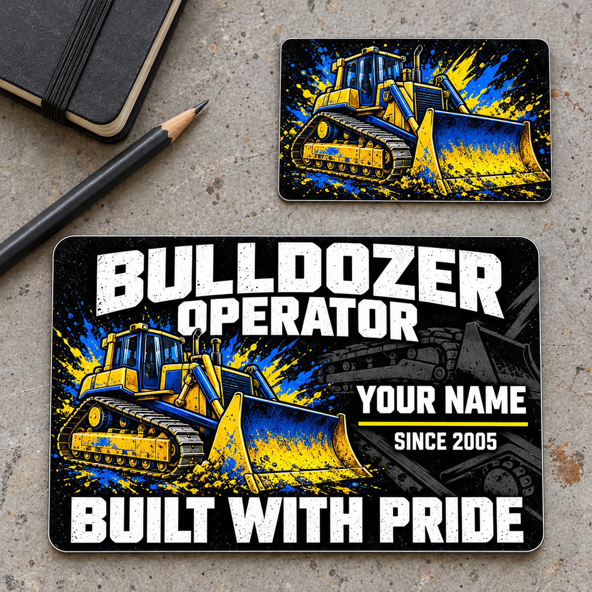 Front and graphic-only reverse of the Bulldozer Operator Midnight Pride aluminum wallet card on a gray planning workbench, with distressed white lettering and vivid blue-and-yellow tracked bulldozer artwork.