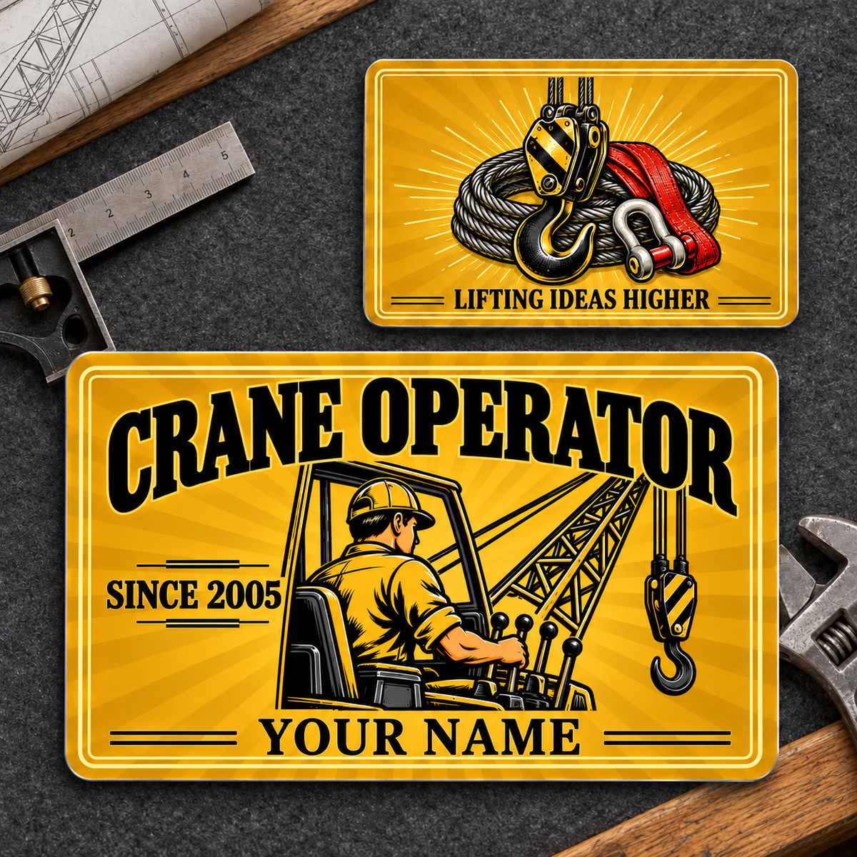 Front and reverse views of one Crane Operator Golden Milestone aluminum wallet card on a crane planning workbench, with golden sunburst artwork and illustrative SINCE 2005 and YOUR NAME text.