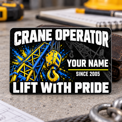 Front of the Crane Operator Midnight Pride aluminum wallet card standing on a gray planning desk, with distressed white lettering and vivid blue-and-yellow crane boom and lifting-hook artwork.