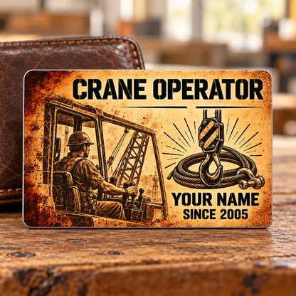Front of the Crane Operator Sepia Legacy aluminum wallet card standing on a timber workbench, with sepia crane-cab operator artwork, a hoist hook, wire rope and shackle, plus illustrative YOUR NAME and SINCE 2005 text.