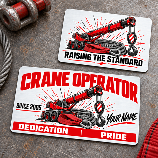 Front and reverse of the Crane Operator Signature Modern aluminum wallet card on a gray workbench, with red and graphite crane, hook, wire-rope and sling artwork, illustrative name and year, Dedication and Pride footer, and Raising the Standard reverse.