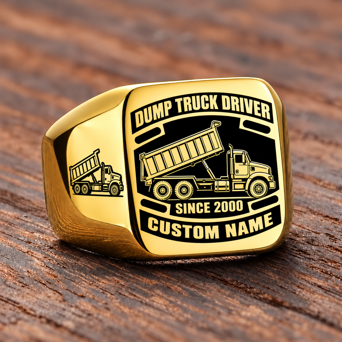 Gold-finish Dump Truck Driver Black Face Badge ring with high-sided tipping-bed truck artwork, matching shoulder truck, and illustrated CUSTOM NAME and SINCE 2000 text