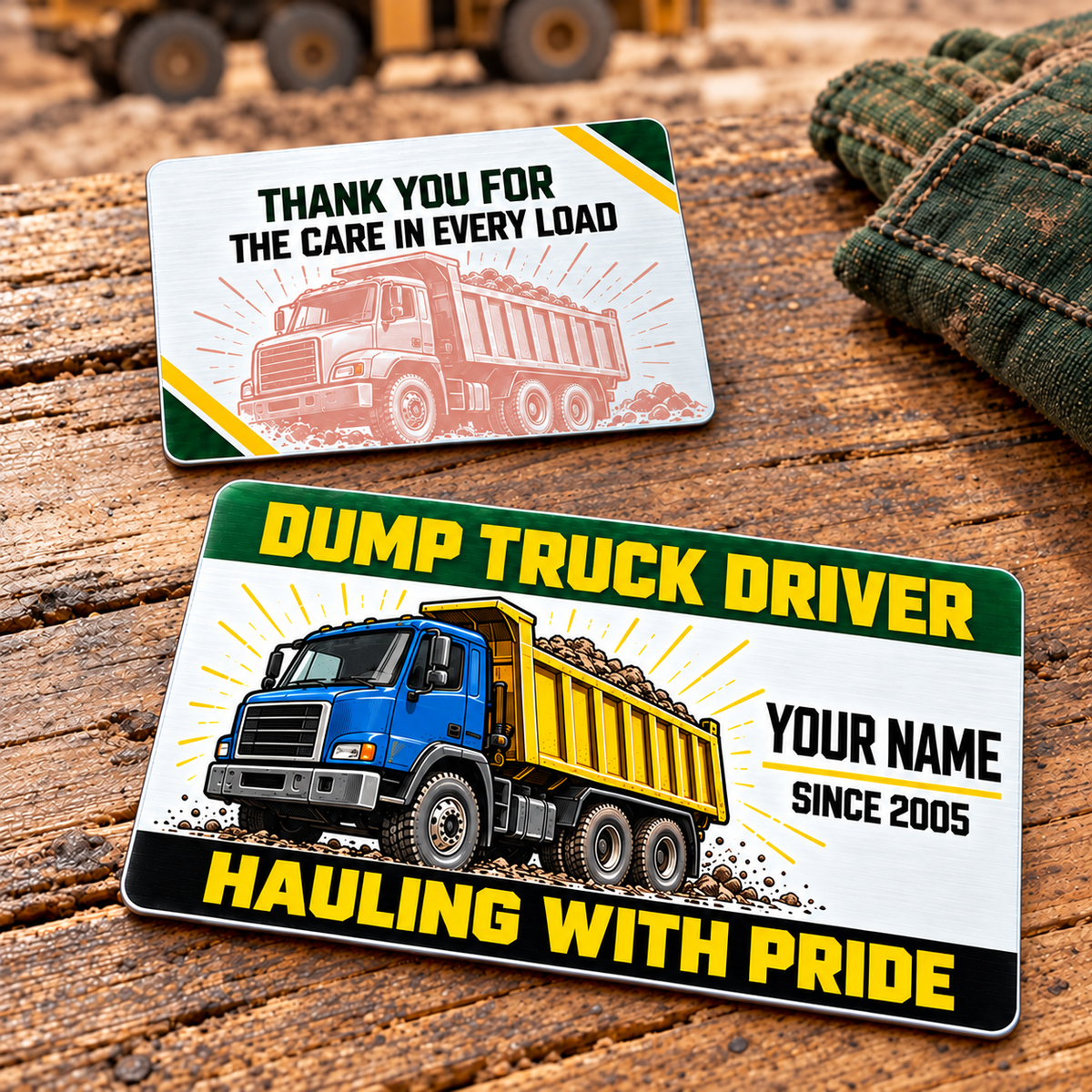 Front and reverse of the Dump Truck Driver Green Band aluminum wallet card, with a green header, yellow lettering, blue-and-yellow rigid dump truck and pale truck illustration on the reverse, resting on a timber tabletop.