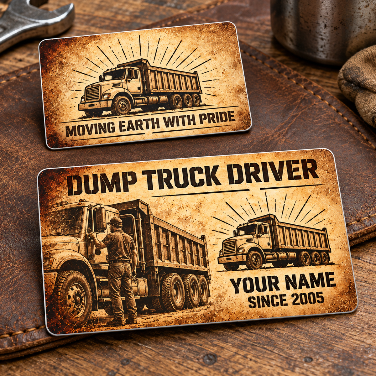 Front and reverse of the Dump Truck Driver Sepia Legacy aluminum wallet card on a brown leather workmat, with parchment-style sepia printing, stencil lettering, a driver beside a parked rigid dump truck and matching truck emblems.