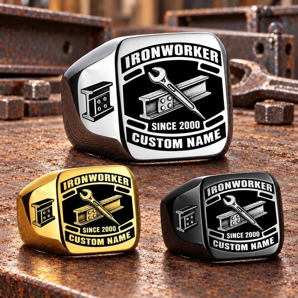 Ironworker Black Face Badge rings in Silver, Gold and Black, with a dominant Silver ring above two smaller finishes on a stationary structural-steel tabletop; sample CUSTOM NAME and SINCE 2000 text