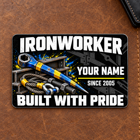 Ironworker Midnight Pride aluminum wallet card front on a brown leather mat, with distressed white lettering and blue-yellow spud wrench, I-beams, bolts and lifting sling artwork.