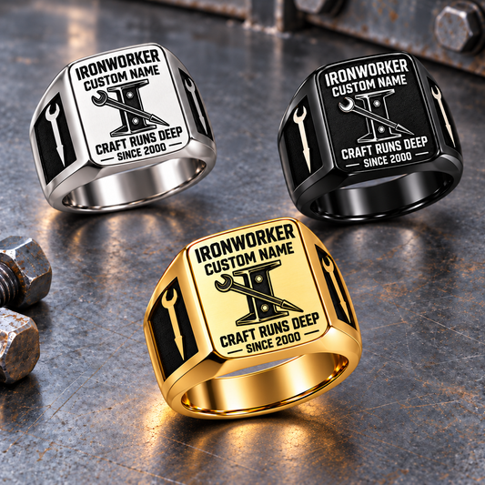 Ironworker Craft Runs Deep signet rings arranged in a triangle on a stationary structural-steel tabletop, with Gold in front, Silver upper left and Black upper right