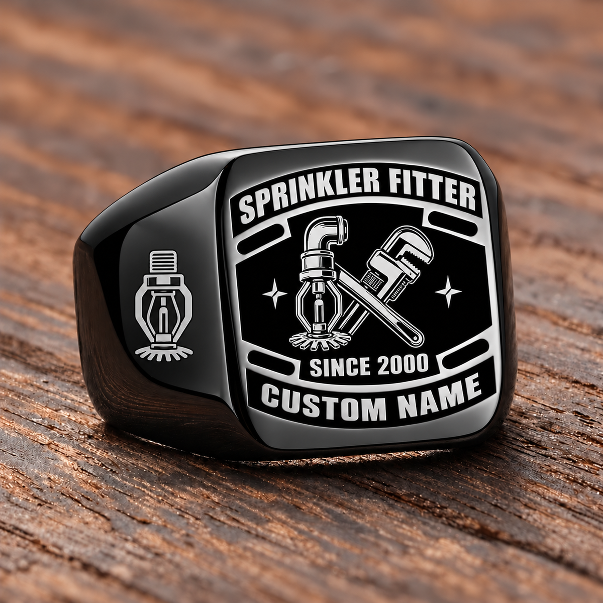 Black-finish Sprinkler Fitter Black Face Badge ring with fire-sprinkler head, pipe and wrench artwork, shoulder sprinkler emblem and illustrated CUSTOM NAME and SINCE 2000 text