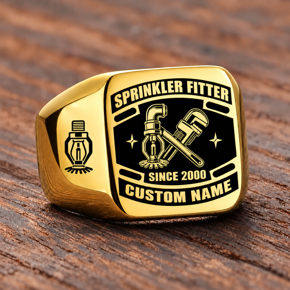 Gold-finish Sprinkler Fitter Black Face Badge ring with fire-sprinkler head, pipe and wrench artwork, shoulder sprinkler emblem and illustrated CUSTOM NAME and SINCE 2000 text