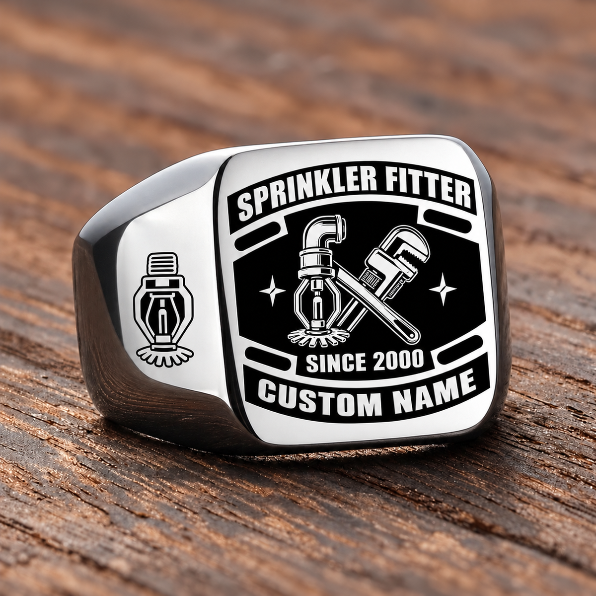 Silver-finish Sprinkler Fitter Black Face Badge ring with fire-sprinkler head, pipe and wrench artwork, shoulder sprinkler emblem and illustrated CUSTOM NAME and SINCE 2000 text