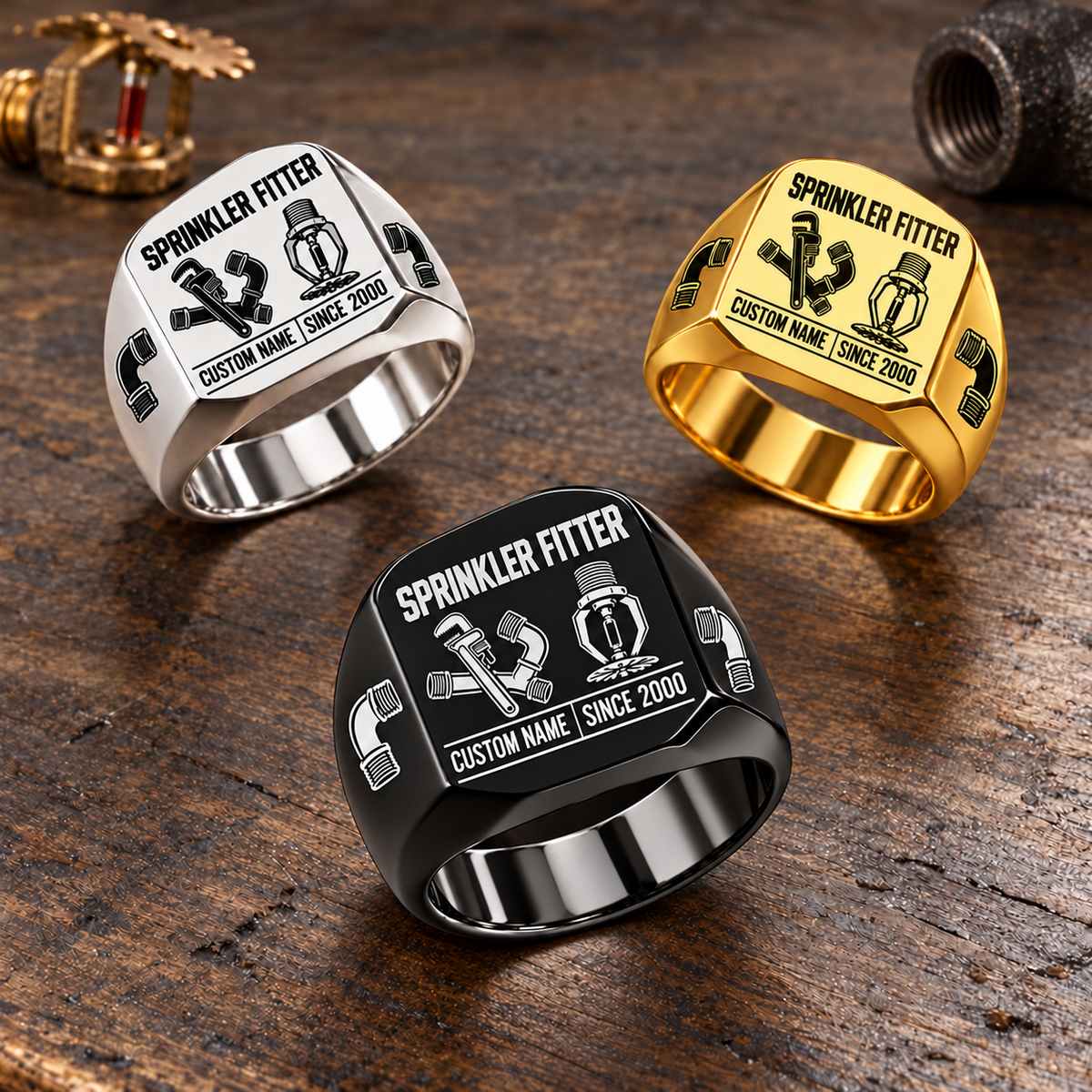 Sprinkler Fitter Twin Icons signet rings in a Black-led triangular arrangement with Silver and Gold on a stationary fire-sprinkler fitting workbench