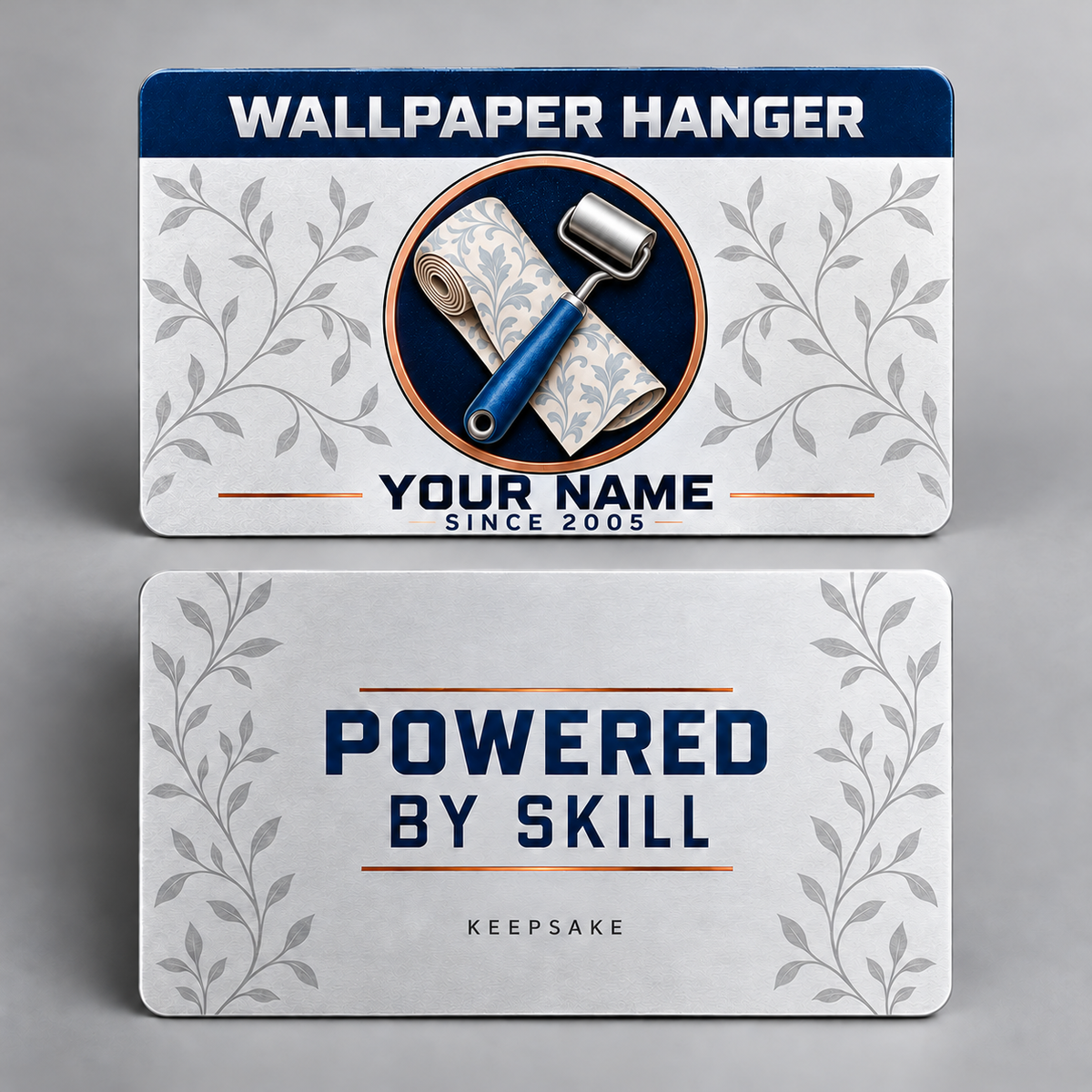 Front and reverse of the Wallpaper Hanger Everyday Craft aluminum wallet card. A plain navy occupation header, wallpaper roll and blue-handled seam roller, silver leaf vines and copper rules accompany YOUR NAME sample text and POWERED BY SKILL with KEEPSAKE on the reverse.