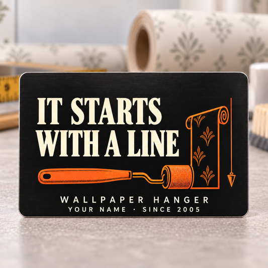 Upright black Wallpaper Hanger aluminum wallet card with cream It Starts with a Line lettering, orange seam roller, wallpaper roll and plumb line.
