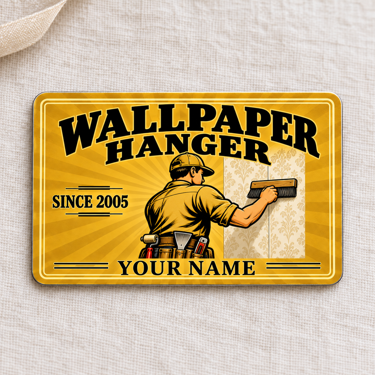 Wallpaper Hanger Golden Milestone aluminum wallet card front on cream linen, showing a worker smoothing wallpaper and illustrative SINCE 2005 and YOUR NAME text.