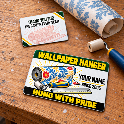 Front and reverse of one Wallpaper Hanger Green Band aluminum wallet card displayed diagonally on a wallpaper workbench; green and yellow header, floral wallpaper roll, seam roller and rule. Name and year are illustrative design text.