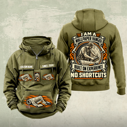 Wallpaper Hanger Heritage Crest Vintage Hoodie in Military Green, source-faithful front and back views with an ornate trade portrait crest, matching chest and pouch badges, and illustrative CUSTOM NAME and SINCE 2000 samples.