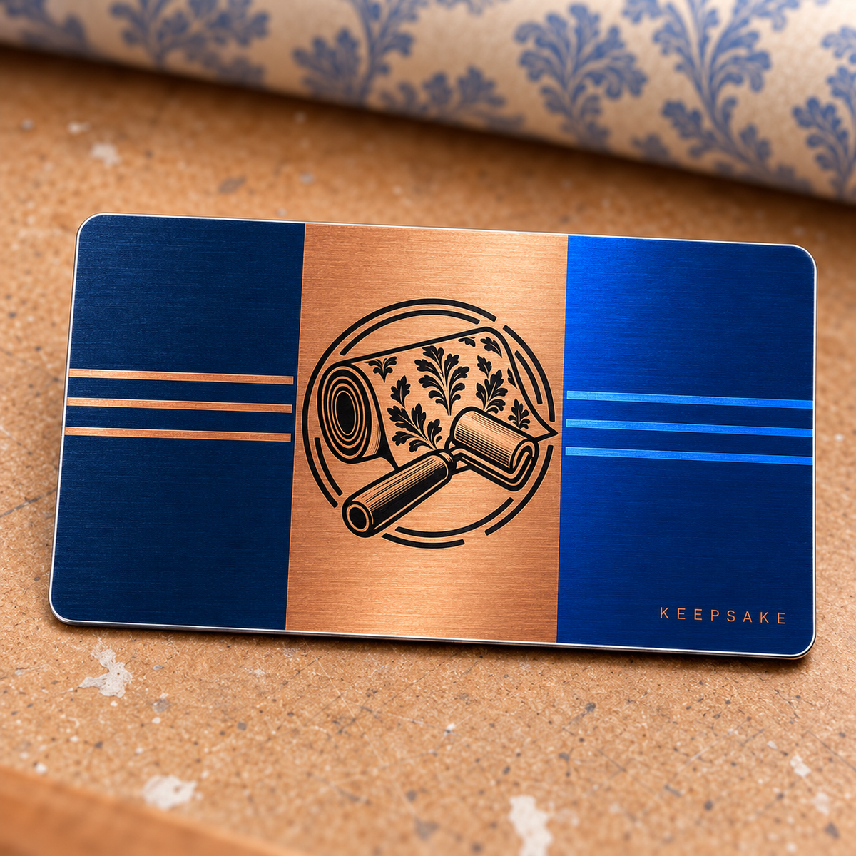 Overhead reverse view of the Wallpaper Hanger Midnight Pride aluminum wallet card, with fine brushed metallic navy and blue side panels, a copper central stripe, black wallpaper roll and seam roller emblem, straight decorative stripes and KEEPSAKE lettering.