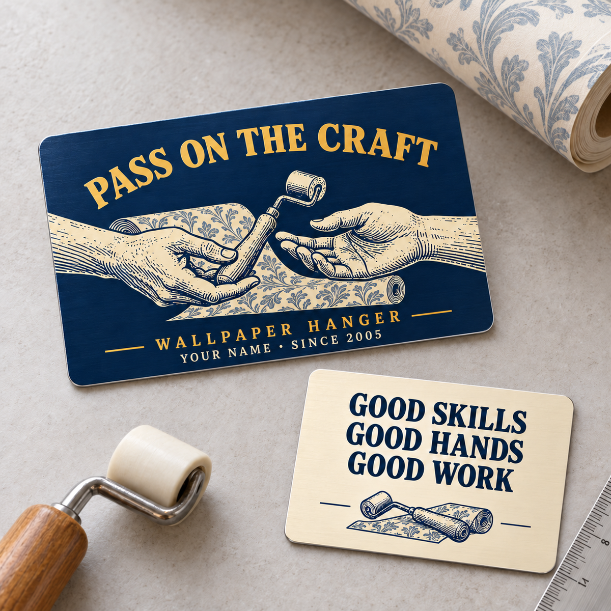 Wallpaper Hanger Pass on the Craft two-sided aluminum wallet card, with navy front and cream reverse arranged diagonally on a wallpaper worktable.