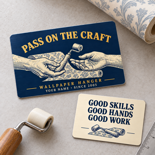 Wallpaper Hanger Pass on the Craft two-sided aluminum wallet card, with navy front and cream reverse arranged diagonally on a wallpaper worktable.