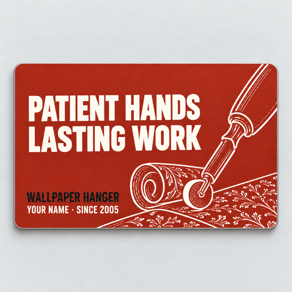 Brick-red front of the Wallpaper Hanger Patient Hands aluminum wallet card, with Patient Hands, Lasting Work lettering and wallpaper roll and seam roller line art.