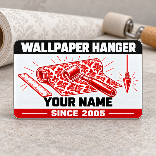 Wallpaper Hanger Red Monochrome aluminum wallet card standing upright on a wallpaper work surface, front artwork with a patterned wallpaper roll, seam roller, ruler and plumb bob.