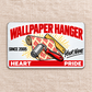 Front of the Wallpaper Hanger Signature Classic aluminum wallet card on linen, with red heading, patterned wallpaper roll, seam roller and ruler, and illustrative name and year text.