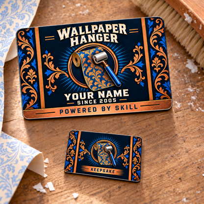 Front and smaller reverse view of one Wallpaper Hanger Toolmark Heritage aluminum wallet card on a wallpaper workbench. Navy, copper and blue damask artwork frames a patterned wallpaper roll and blue-handled seam roller; the front shows illustrative YOUR NAME and POWERED BY SKILL text.