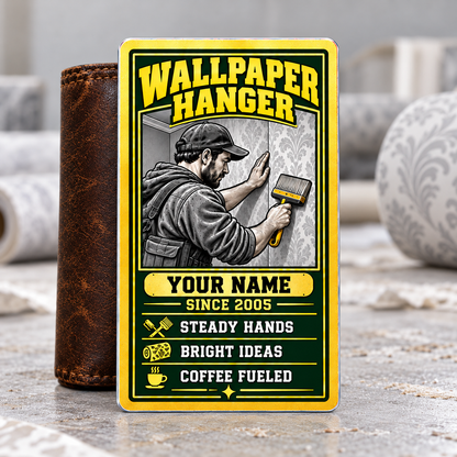 Wallpaper Hanger Trade Legend aluminum wallet card, portrait front with green-and-gold artwork, supported by a brown wallet on a wallpapering table