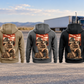 Five complete back views of the Trucker Ready Every Day Portrait Vintage Hoodie, left to right Military Green, Kaki, Dark Gray, Black and Dark Blue, arranged separately before a parked unbranded truck and open-road landscape. Each has the same compact road-and-truck panel above a larger kneeling trucker beside a travel bag.