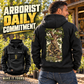 Black Arborist Daily Commitment Portrait Vintage Hoodie worn off-duty at a tree nursery, showing the kneeling-arborist tree graphic on the back and a smaller front view with CUSTOM NAME and SINCE 2000.