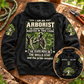 Black Arborist Skills and Pride Vintage Hoodie on a warm workshop bench, with a large readable back statement and arborist portrait plus a small front-detail inset.