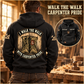 Black Carpenter Walk the Walk Badge hoodie with boot artwork, shown from the back in a warm workshop with a smaller front-view inset.