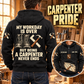 Black Carpenter Never Ends hoodie, dominant back view with boots and carpenter tool artwork in a warm woodworking shop, plus smaller front view.