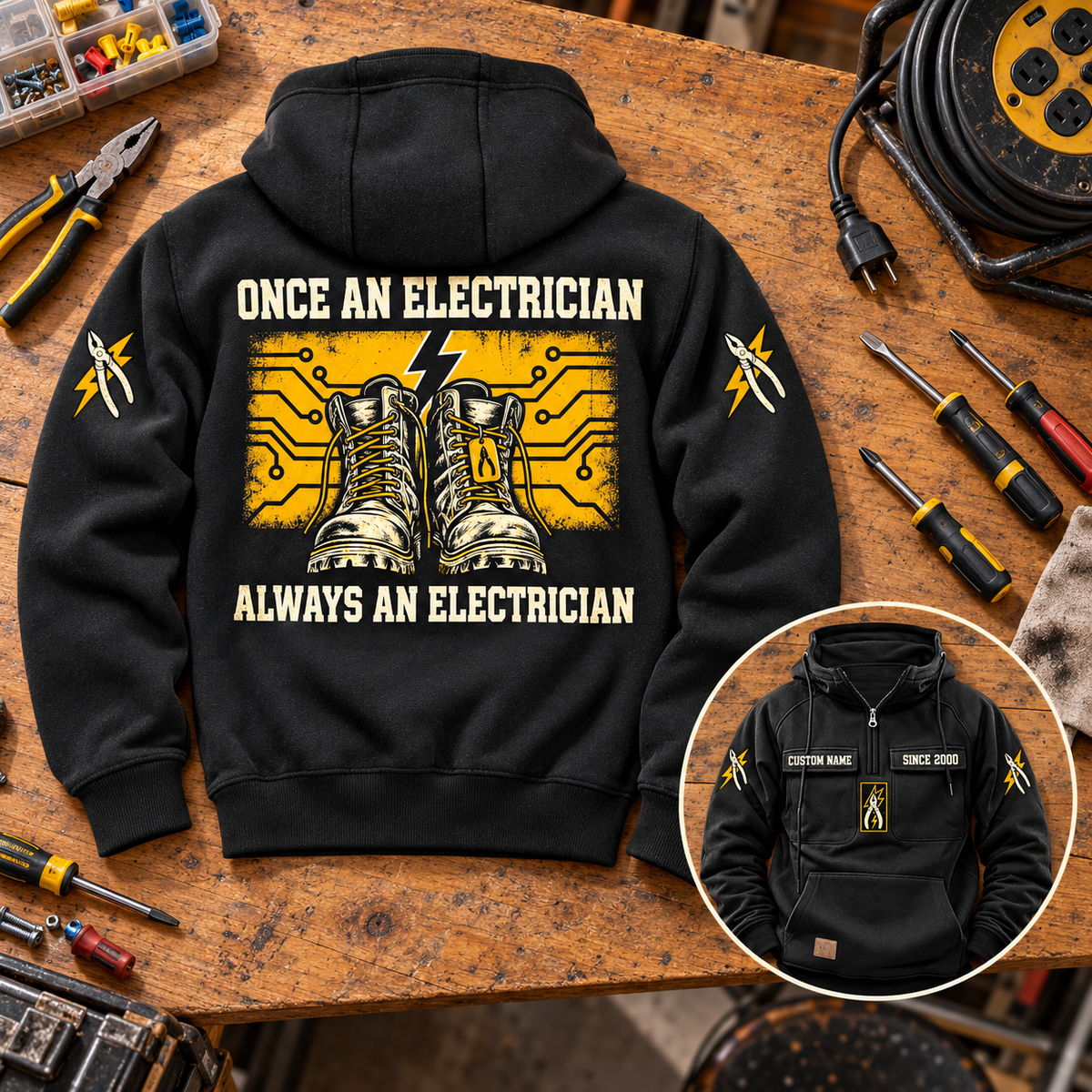 Black Electrician Once and Always Vintage Hoodie laid back-up on an electrician workbench with boots and circuit artwork, unplugged cable reel and a smaller front view showing CUSTOM NAME and SINCE 2000.