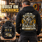 Black Electrician Heritage Crest Vintage Hoodie worn from the back in a warmly lit workshop, showing the cream and gold electrician crest and NO SHORTCUTS text, with a smaller front view showing CUSTOM NAME, SINCE 2000 and tool graphics.