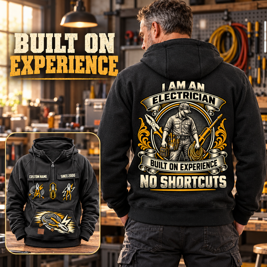 Black Electrician Heritage Crest Vintage Hoodie worn from the back in a warmly lit workshop, showing the cream and gold electrician crest and NO SHORTCUTS text, with a smaller front view showing CUSTOM NAME, SINCE 2000 and tool graphics.