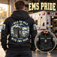 Black EMS Walk the Walk Badge Vintage Hoodie on a back-view model beside a parked ambulance, with I WALK THE WALK / WITH EMS PRIDE boot artwork and a smaller front-view inset.